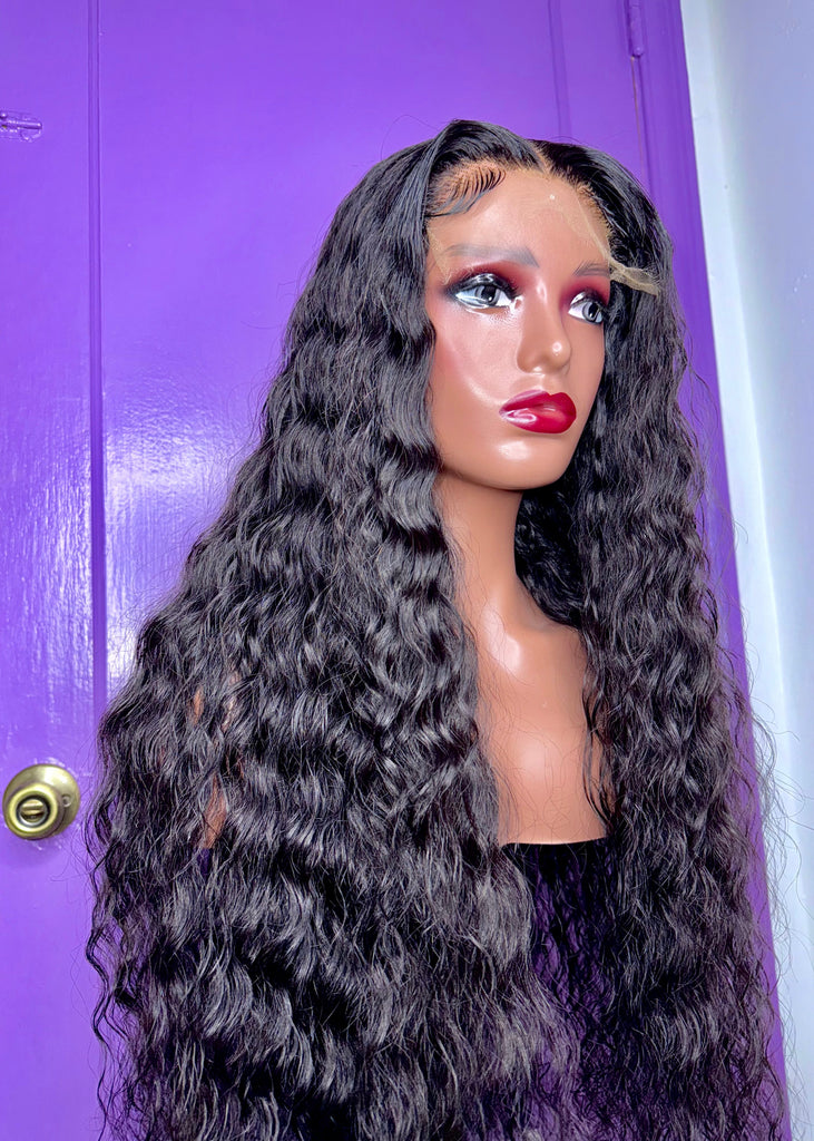 A mannequin head displaying a wig with long, wavy hair, wearing a purple outfit with a matching purple door in the background.